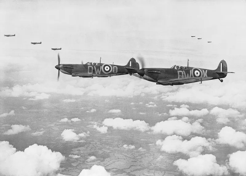 Three early Spitfires flying close together in a V formation above fields
