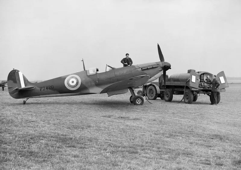 A Spitfire being refuelled on a grass airfield by ground crew