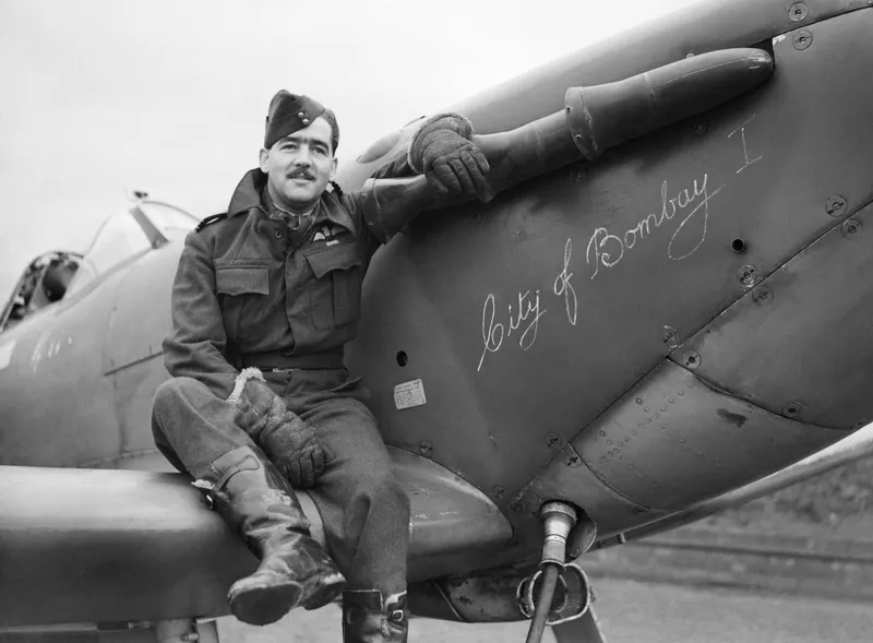 A Spitfire Mk V parked on an airfield with a pilot beside it