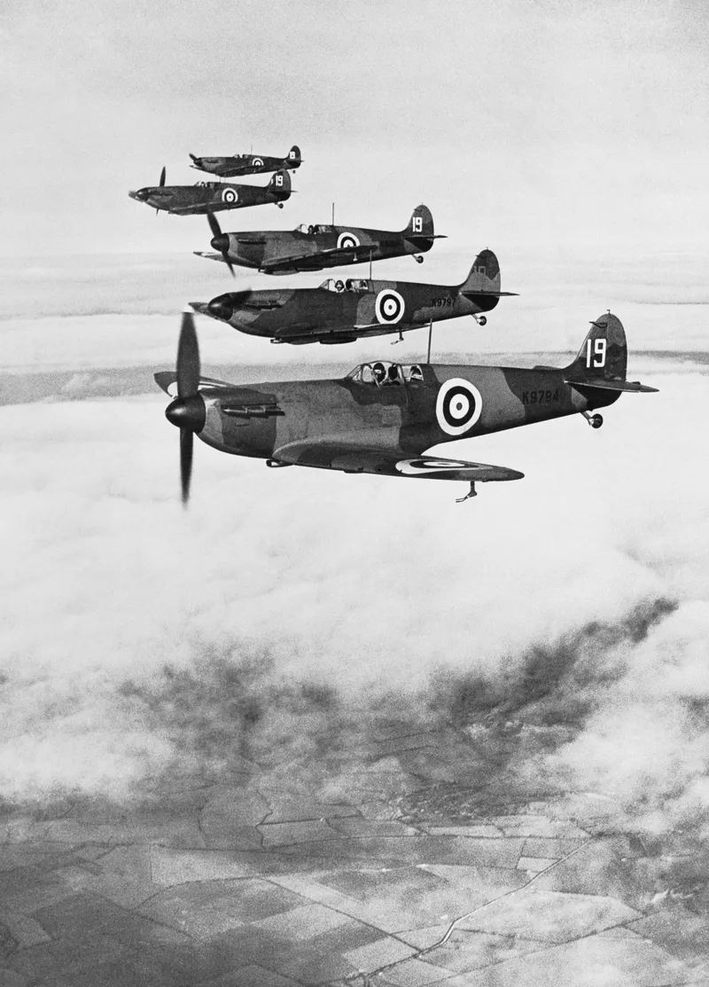 A formation of early Spitfires flying over flat farmland